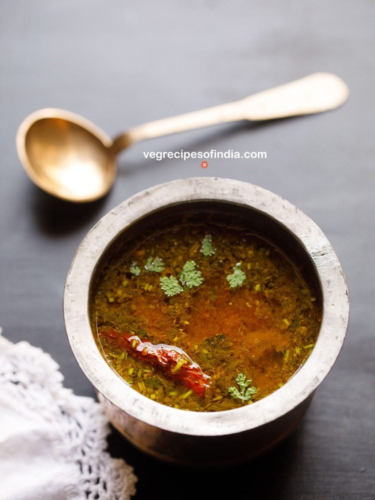 tomato rasam in a traditional South Indian container with a spoon placed on top