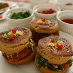 side shot of dabeli served on a white plate with garnished kept in white bowls on the upper side.