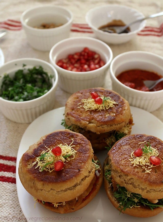 prepared dabelis served on a plate with garnishes and chutney kept in bowls on the side. 