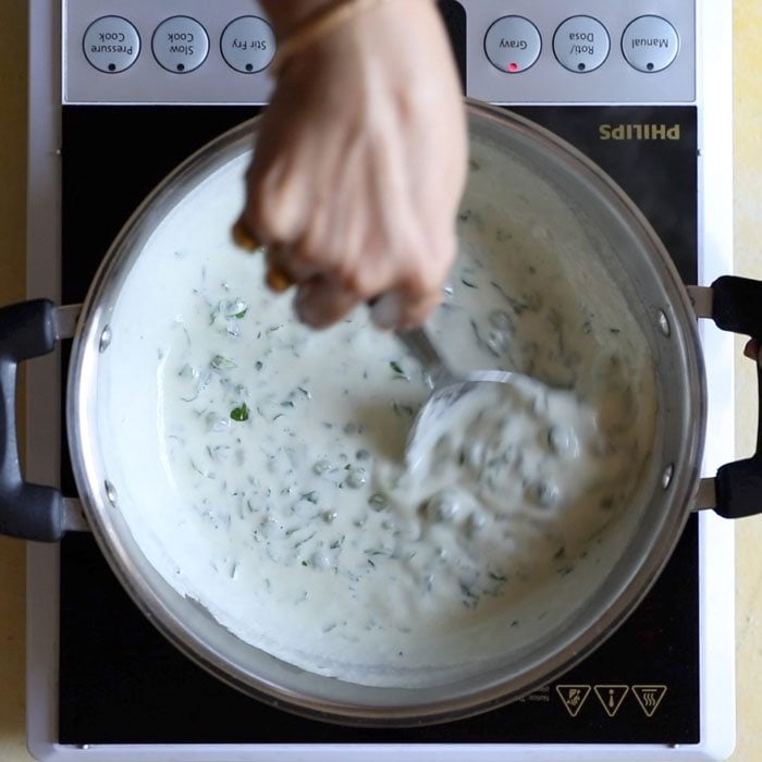 mixing in the cream and peas into the methi matar malai recipe.