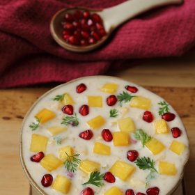 pineapple raita garnished with fresh pomegranate arils in a hand-thrown earthenware bowl with matching plate.