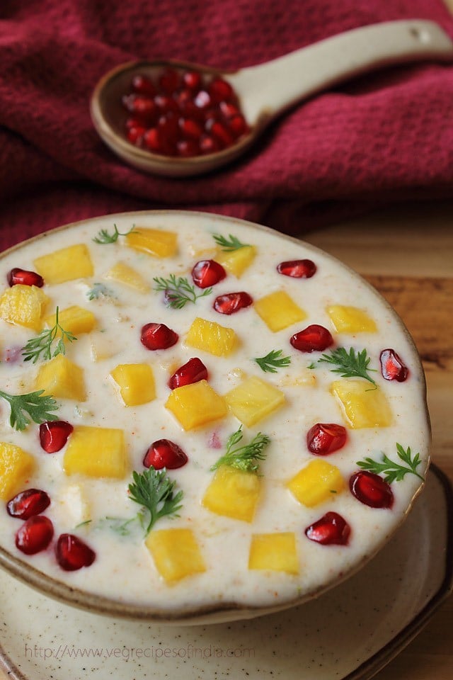 pineapple raita garnished with fresh pomegranate arils in a hand-thrown earthenware bowl with matching plate.