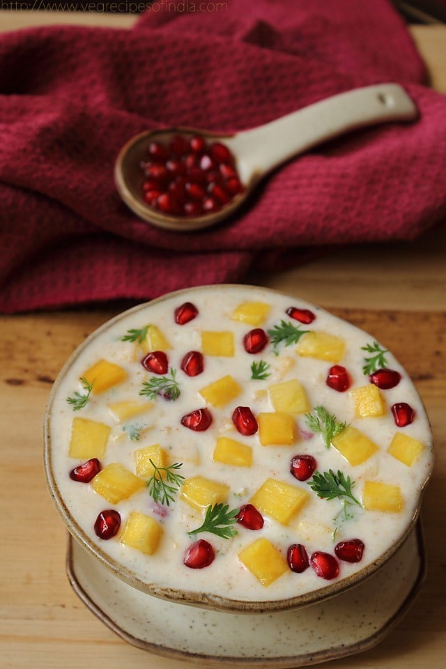 pineapple raita garnished with fresh pomegranate arils in a hand-thrown earthenware bowl with matching plate.