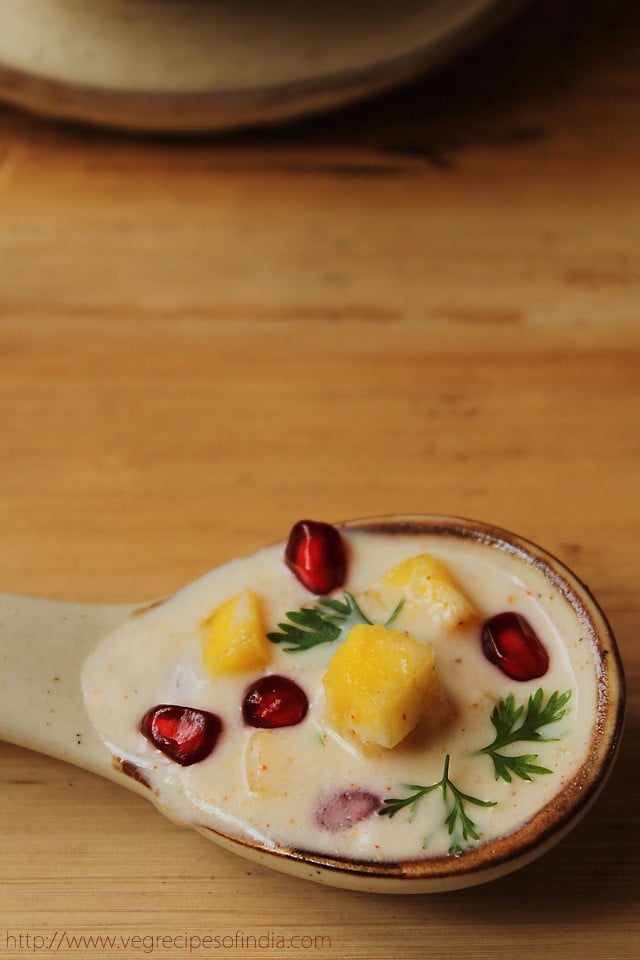 close up shot of an earthenware spoon full of pineapple raita on a wooden table.