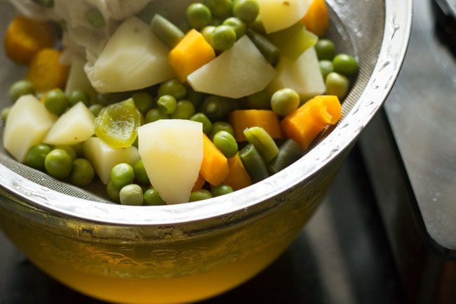 strainer filled with vegetables on top of glass bowl filled with stock 