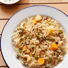 top shot of yakhni pulao garnished with fried onions and cashews in a white plate.