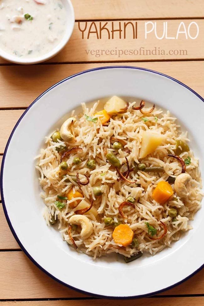 top shot of yakhni pulao garnished with fried onions and cashews in a white plate.