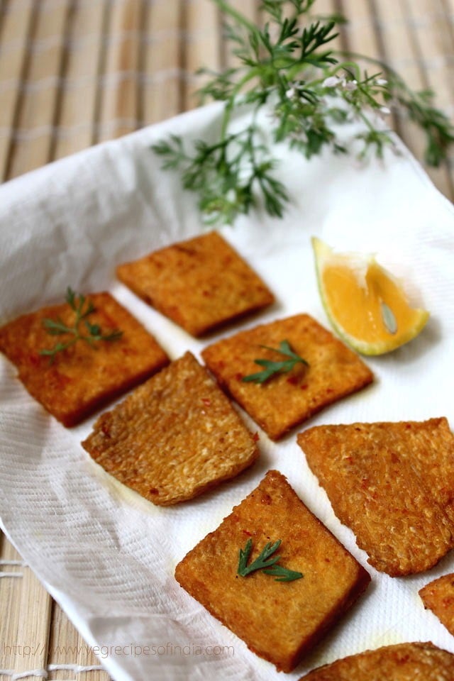 yam chips garnished with coriander leaves, placed on a kitchen paper towel with a piece of lemon kept on the side. 