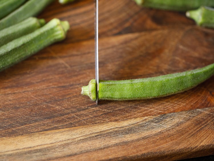 chopping bhindi crown with a knife.