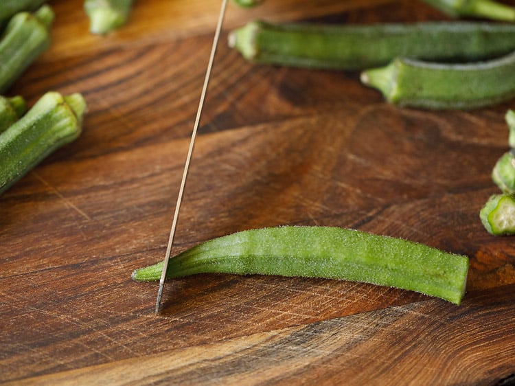 chopping bhindi base tip with a knife.