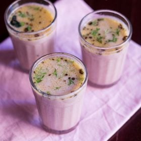 three clear glasses of solkadhi on a pink napkin.