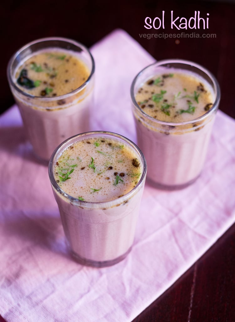 three clear glasses of solkadhi on a pink napkin.