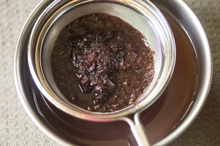 pouring the kokum soak through a mesh strainer.