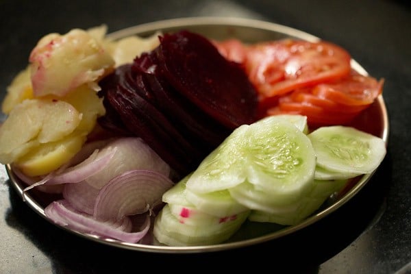 sliced tomatoes, cucumber, onions, boiled potatoes and beetroot on a plate.