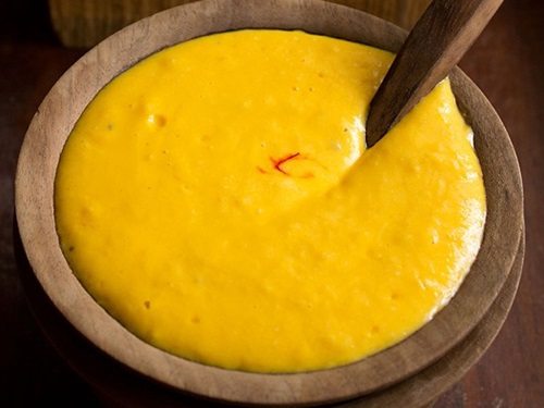 mango shrikhand in a wooden bowl with wooden spoon inside