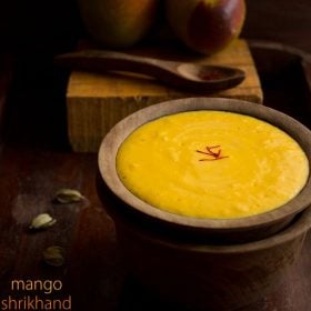 mango shrikhand in wooden bowl with fresh mangoes in the background