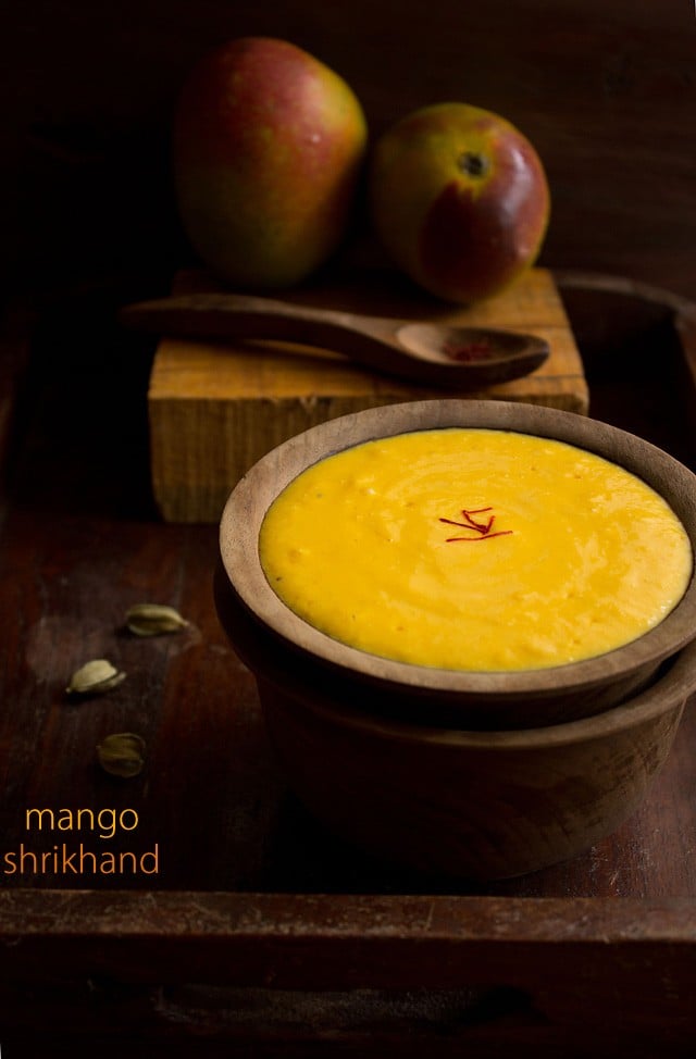 mango shrikhand in wooden bowl with fresh mangoes in the background