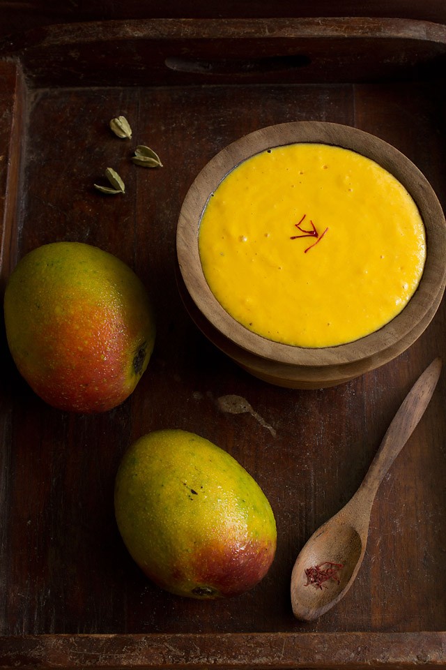 mango shrikhand served in a wooden bowl with fresh ripe mangoes on a wooden tray