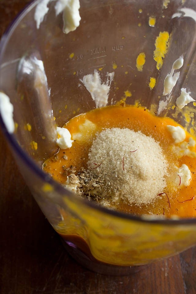 adding hung curd, sugar, crushed green cardamoms and saffron in blender jar 