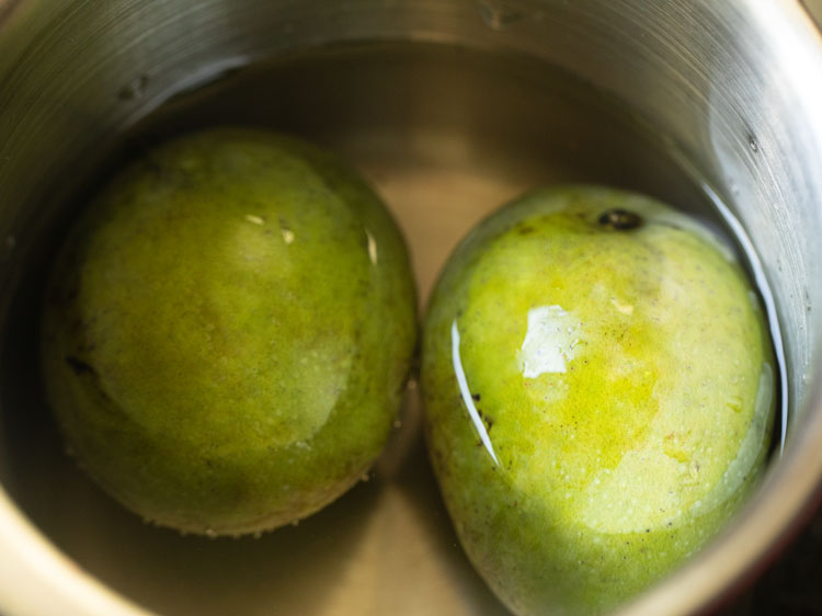 cooking two green mangoes in water for making aam panna.