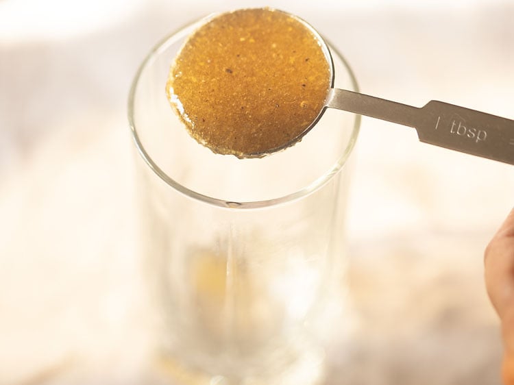 tablespoon of aam panna concentrate being added to a highball glass.