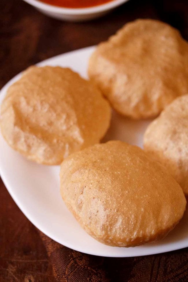 4 golden brown puris on a white plate for serving aloo poori. 