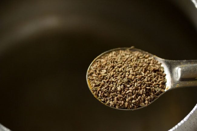 adding ajwain (carom seeds) to hot oil in a pressure cooker.