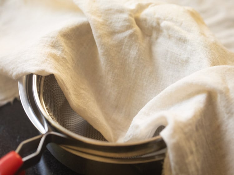 strainer on top a bowl with a muslin  cloth on top of strainer to set paneer