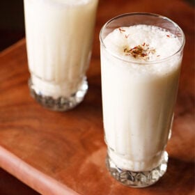 sweet lassi topped with crushed cardamom powder and saffron in two tall glasses