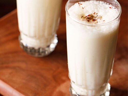 sweet lassi topped with crushed cardamom powder and saffron in two tall glasses