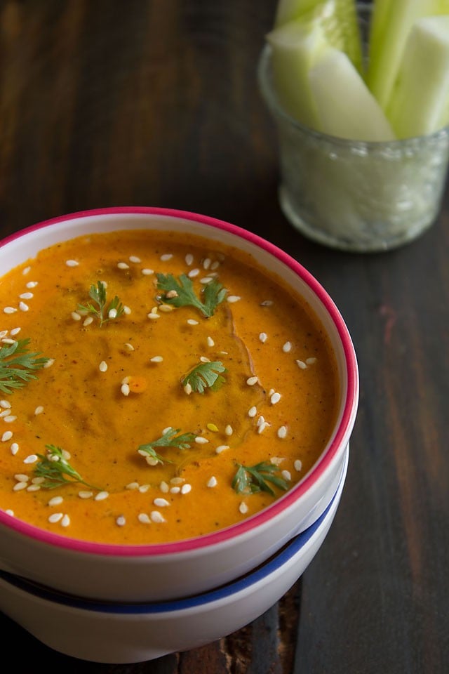 muhammara dip in a bowl with a glass of fresh cut veggies in the background for dipping.