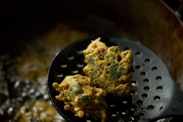 fried palak pakoda on a black slotted spoon