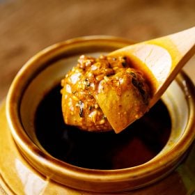 punjabi mango pickle scooped in a wooden spoon on top of a ceramic jar placed on a brown wooden board