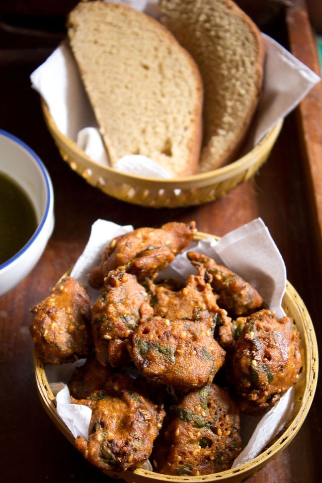 palak pakoda served in a bowl with a side of wheat bread slices and coriander chutney on a wooden board.