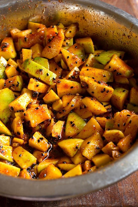 mixing spices with the mango pieces in the steel bowl for  meetha aam ka achar