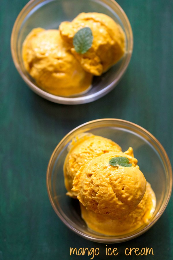 scoops of mango ice cream in two glass bowls garnished with a mint leaf on a green board