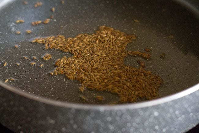 cumin seeds spluttering in hot oil in pan for making sabut masoor dal. 
