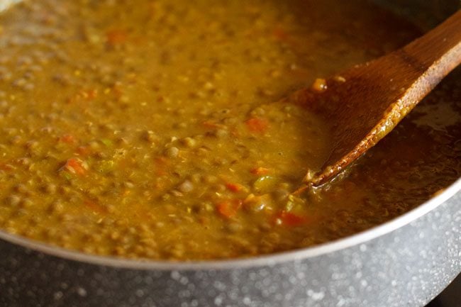 mashing some red lentils with a ladle. 