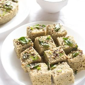cuadrados de moong dal dhokla servidos en un plato blanco.