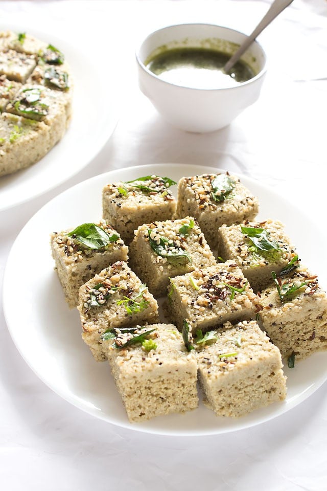 moong dal dhokla squares served on a white plate.