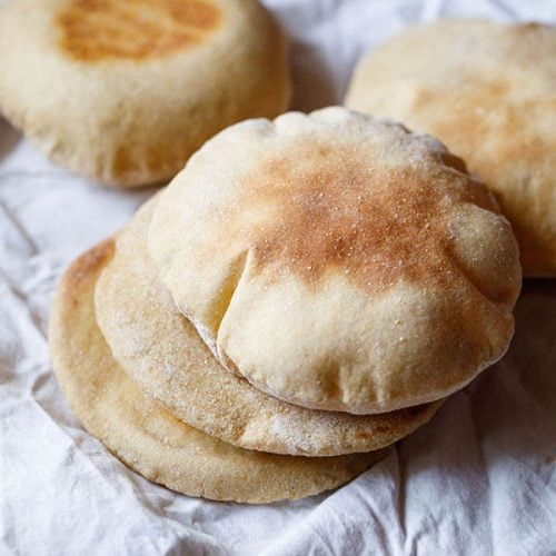 whole wheat pita bread stacked with 2 pita bread in the background placed on a white cotton napkin