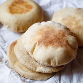 whole wheat pita bread stacked with 2 pita bread in the background placed on a white cotton napkin