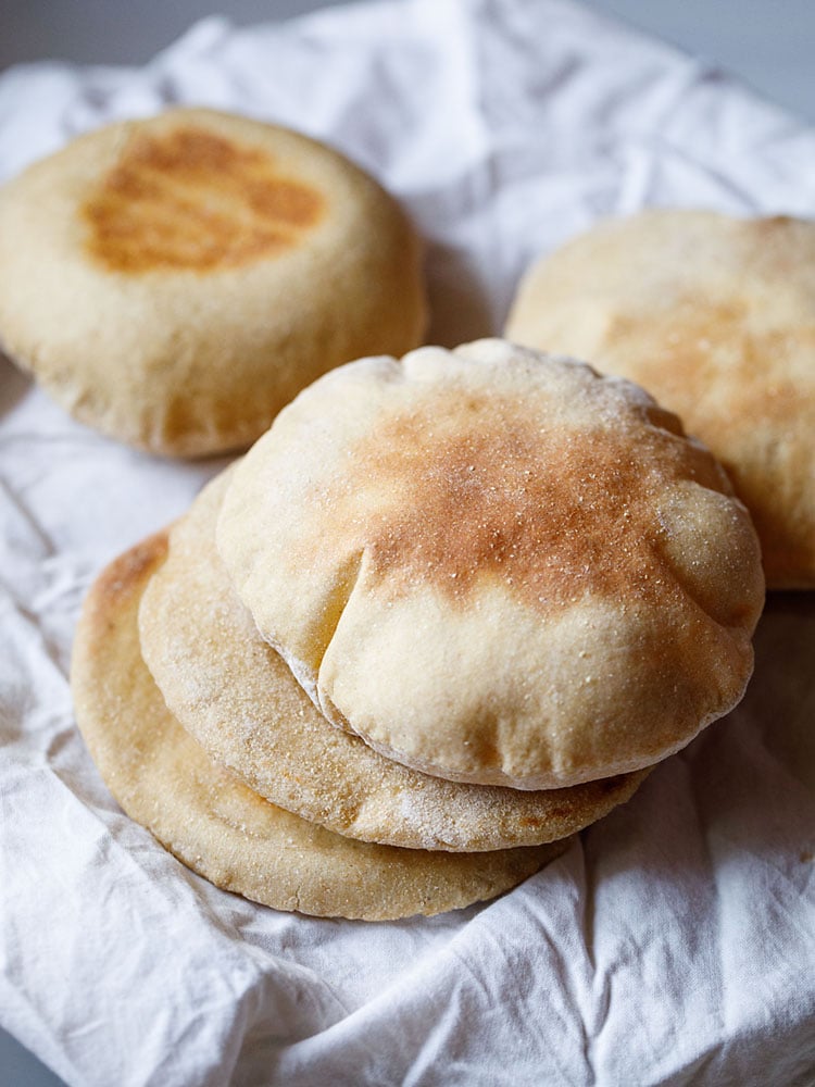 whole wheat pita bread stacked with 2 pita bread in the background placed on a white cotton napkin