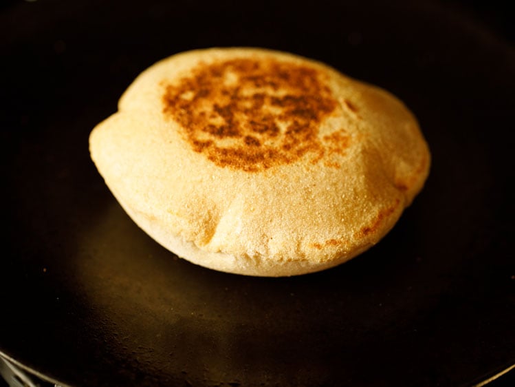 puffed up pita bread flipped over and the second side being roasted