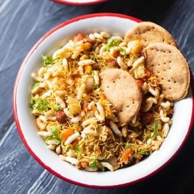 bhel puri served with a side of crisp baked puri in a red rimmed white bowl