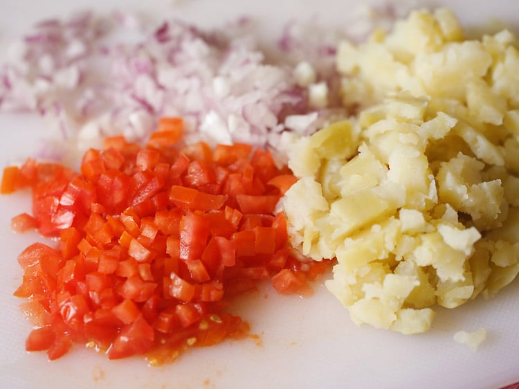 chopped onions, tomatoes, boiled potatoes on a white chopping board