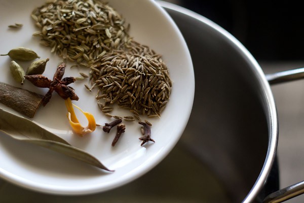 whole spices being added from a white plate into the pot