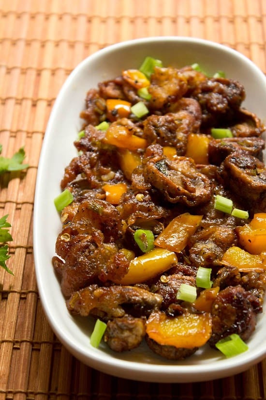 dry mushroom manchurian in an oblong white dish garnished with fresh cut scallion greens.