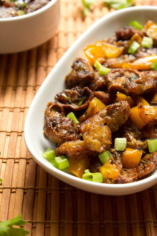 dry mushroom manchurian in a white bowl on a table with a bamboo placemat.