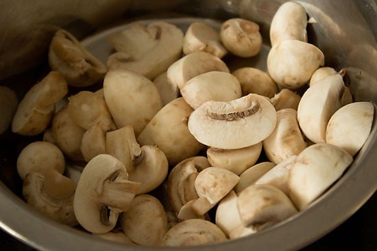 halved button mushrooms in a silver prep bowl.